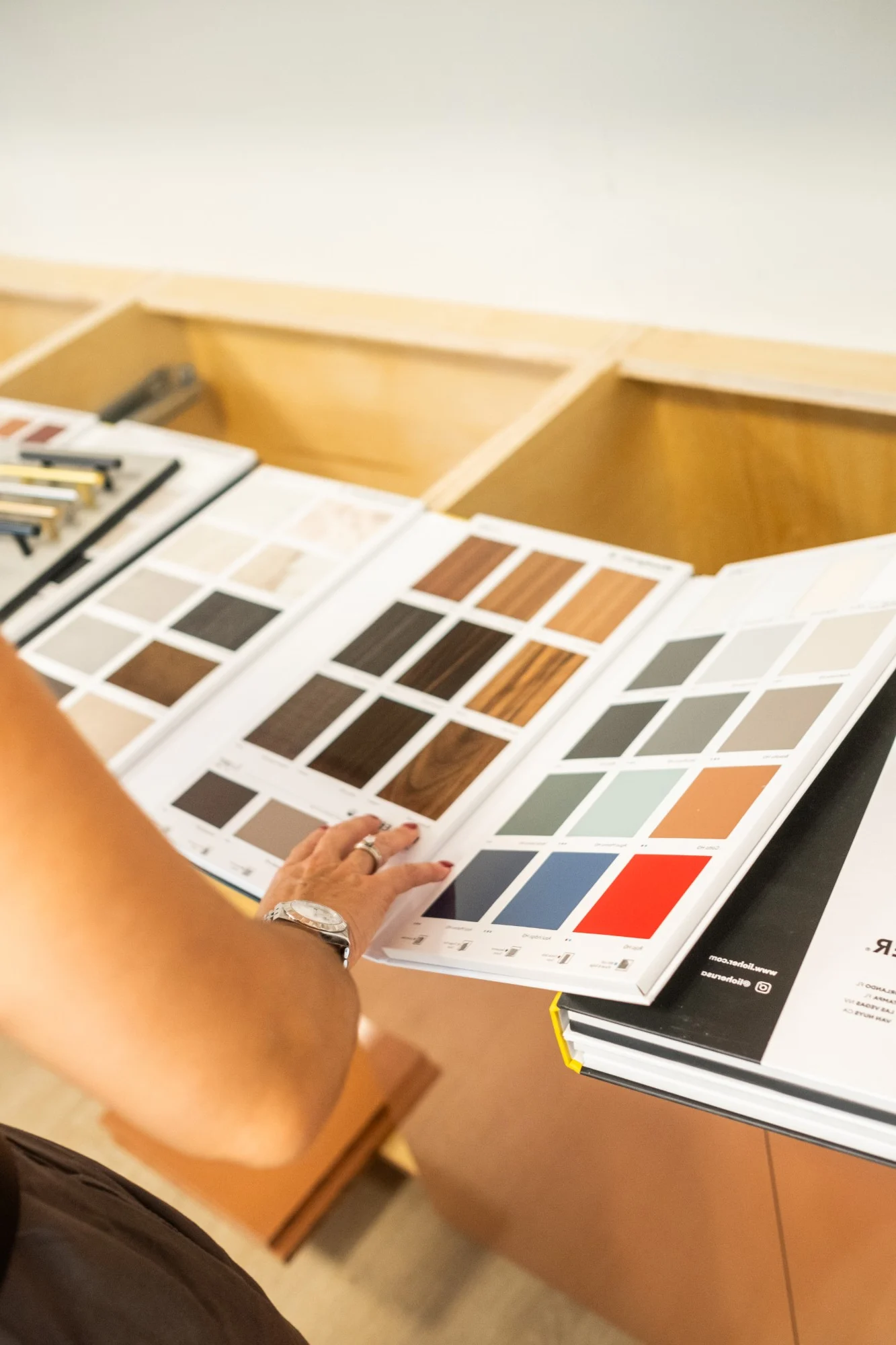 Designer paging through finish and veneer sample binders beside plywood cabinet boxes